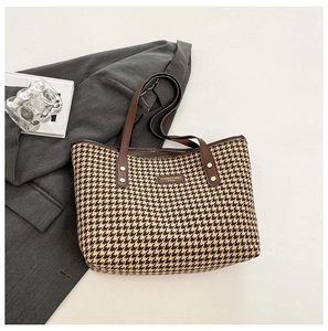 Detail of classic houndstooth tote bag with brown leather handles and gold rivet accents