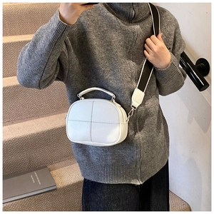Detailed view of white minimalist crossbody bag with cross-stitch seam and wide strap
