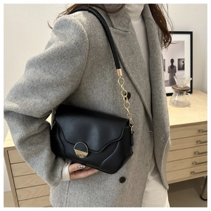 Détail d'un sac bandoulière minimaliste en cuir noir avec chaîne dorée sur veste grise