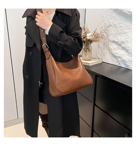 Detail of vintage brown leather tote bag with matte texture on a black trench coat