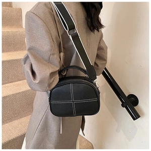 Close-up of black crossbody bag featuring distinct white cross stitching and wide strap