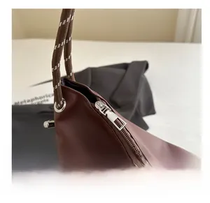 Detail of smooth metal zipper and woven braided strap on dark brown leather tote bag