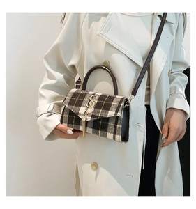 Detail of plaid crossbody bag with gold SS logo and metal tassel on a beige trench coat