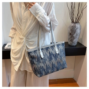 Detail of blue geometric woven tote bag with silver handles worn on shoulder