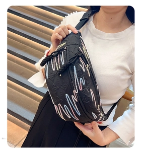Detail of black corduroy dumpling bag featuring colorful wavy embroidery and adjustable strap
