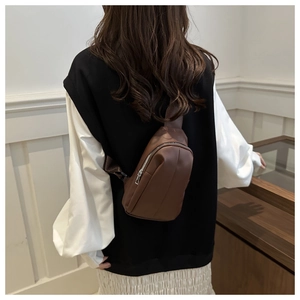 Deep brown leather sling bag worn by a model against a minimalist studio background