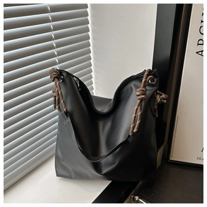 Detail of black tote bag featuring distinctive thick rope handle and metallic ring accents