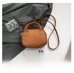 Brown mini bowling bag size comparison with smartphone showing compact leather design