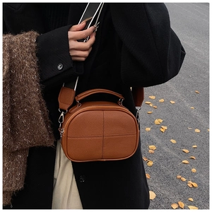 Close-up of brown textured leather shoulder bag with wide woven strap in autumn setting