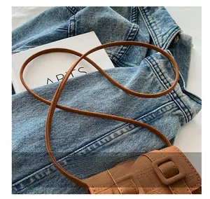 Close-up of comfortable shoulder strap and vintage brown crossbody bag on denim jacket