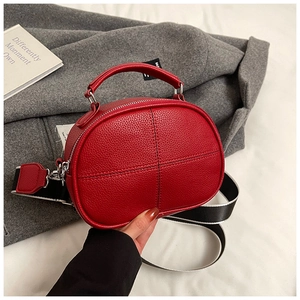 Close-up of red lychee leather bag with cross-stitch details and wide woven strap