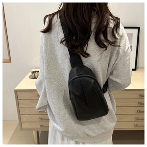 Close-up of minimalist black matte leather crossbody chest bag with silver metal zipper details