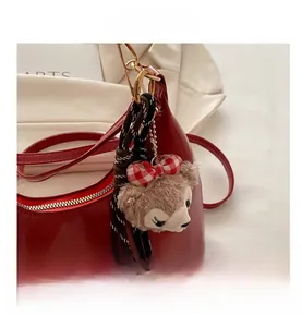Detail of ShellieMay plush charm with red bow on shiny leather dumpling crossbody bag