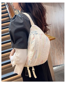 Detail of white corduroy crossbody bag with colorful wavy stitching and braided zippers