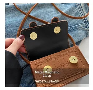 Close-up of brown croc-effect bag with dual golden magnetic snaps on blue denim