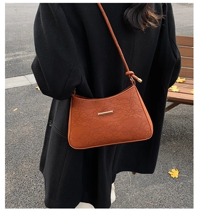Detailed close-up of brown floral embossed underarm bag on black wool coat background