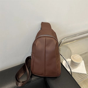 Minimalist brown PU leather crossbody chest bag with adjustable strap on a leather sofa