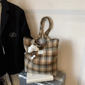 Brown and beige plaid tote bag with cloud charm on silver suitcase in urban setting