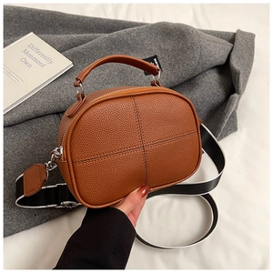 Detailed shot of brown pebble leather bag with cross-stitch and wide canvas strap