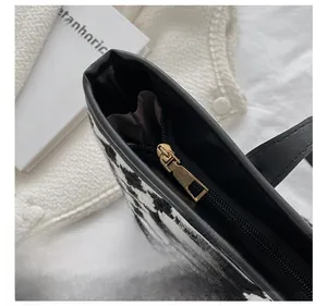 Detailed close-up of golden metal zipper puller on houndstooth tote bag with leather trim