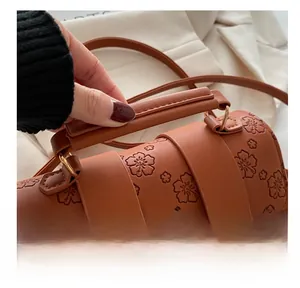 Detail of a brown leather cylinder bag featuring embossed floral patterns and a gold lock