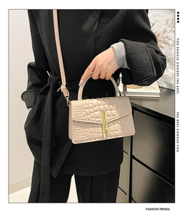 Detail of beige crocodile embossed handbag featuring an elegant gold metal lock clasp