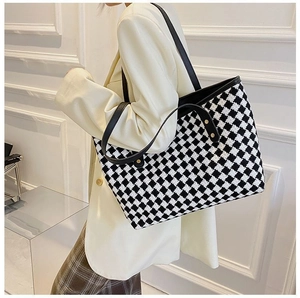 Detail of checkered tote bag with black leather strap worn by a model in soft light