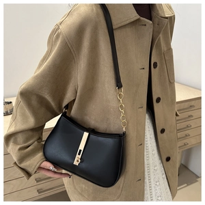 Détail du sac baguette en cuir noir avec boucle dorée et bandoulière en chaîne