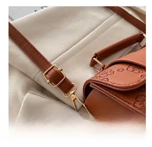 Close-up of adjustable gold buckle on caramel leather handbag with floral embossing