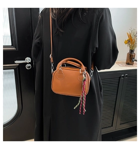 Caramel bowling bag with colorful tassel charm worn over a black winter coat