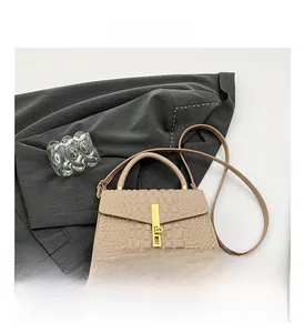 Close-up of beige crocodile-embossed leather handbag with gold metal lock on grey suit