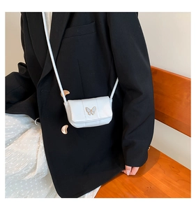 Gros plan d'un mini sac blanc avec détail de papillon doré porté sur un blazer noir