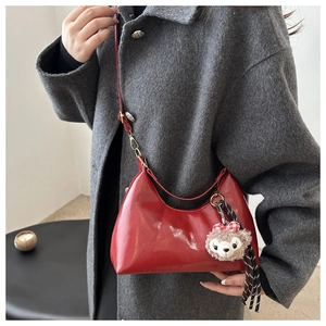 Detail of red wax leather crossbody bag with cute plush pendant and glossy finish on grey coat