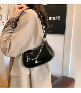 Detail of black patent leather shoulder bag with silver star chain and pearl pendant charm