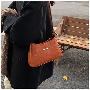 Detail of orange-brown underarm bag featuring floral embossing and gold metal accent