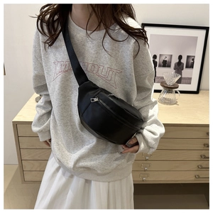 Adjustable black faux leather crossbody waist bag styled on a model in a warm room