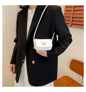 Détail du sac bandoulière blanc matelassé avec boucle papillon dorée porté par un mannequin