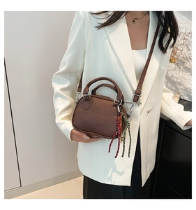 Brown bowling bag for women worn crossbody, showing mini size and texture on white blazer