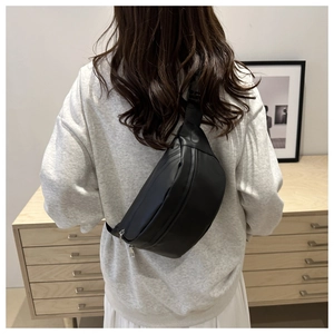 Detail of a black minimalist crossbody chest bag with silver zippers and wide nylon strap