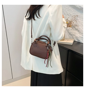 Detail of dark brown leather bowling bag showing adjustable strap and side woven charm