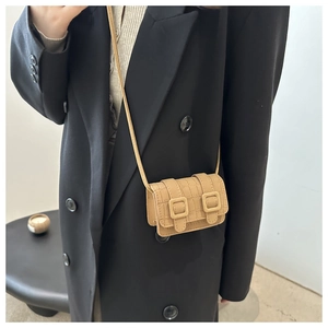 Close-up of beige crocodile pattern texture and square buckle details on a crossbody bag