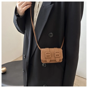Detail of vintage brown textured leather mini crossbody bag with buckle closure on black blazer