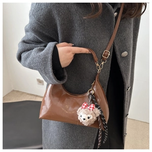 Brown vintage half-moon bag detail with plush bear charm and ribbon on tweed coat