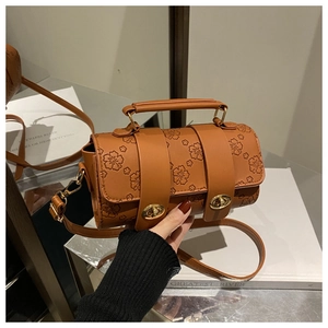 Detail of brown cylindrical Boston bag with embossed cherry blossoms and gold twist-locks
