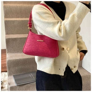 Close-up of rose red underarm bag featuring floral lace embossing and gold metal bar