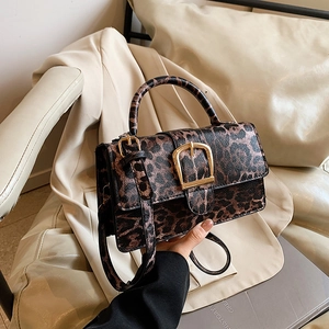 Vintage leopard print crossbody bag with gold buckle and top handle on a warm background