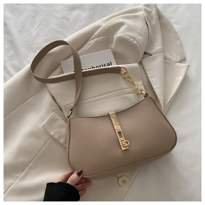 Détail du sac beige avec fermoir doré sur un blazer crème et décor de livre