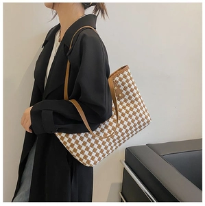 Close-up of checkered woven tote bag with brown leather straps worn by a model in a coat