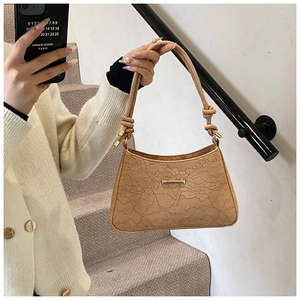 Close-up of beige shoulder bag featuring floral lace embossing and knotted handle detail