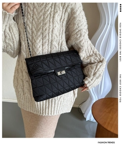 Detail of black quilted shoulder bag with silver turn-lock and leather chain strap